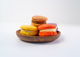 Multicolored macarons on a wooden plate on a white background.