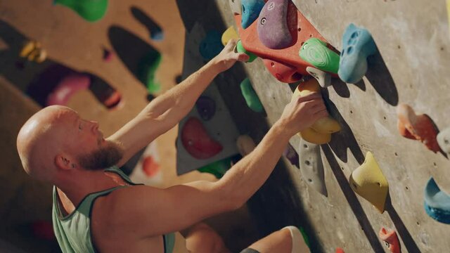 Strong Experienced Rock Climber Practicing Solo Climbing on Bouldering Wall in Gym. Man Exercising at Indoor Fitness Facility, Doing Extreme Sport for His Healthy Lifestyle Training. Close Up Portrait