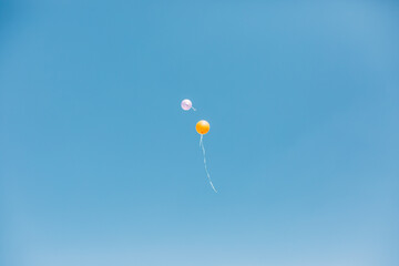 two balloons fly high into the sky. The balls are pink and orange. The sky is blue without a single cloud