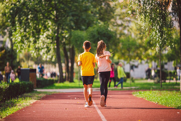 Sports and fitness in adolescence. Caucasian twins boy and girl run on the jogging track in the city park. Two children brother and sister for 10 years running on a rubberized outdoor treadmill