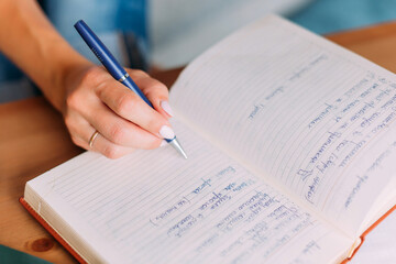 Woman writes down list of business or household chores in notebook. Close-up of hand, notebook and...