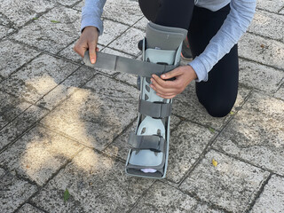 Person adjusting the Velcro of the orthopedic boot ideal for leg injuries, such as bone fracture. Patient walking in the street.