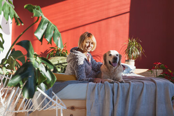 Happy smiling woman and golden retriever puppy dog in bright sunny red walls stylish bedroom with...