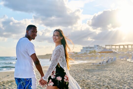 Portrait of happy young multiethnic couple holding hands on the seashore