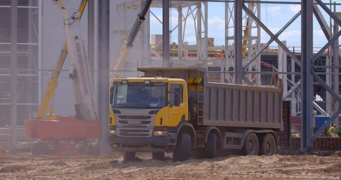 At the construction site of a plant under construction, a large, powerful, multi-axle cargo truck is driving in reverse to the place of loading 