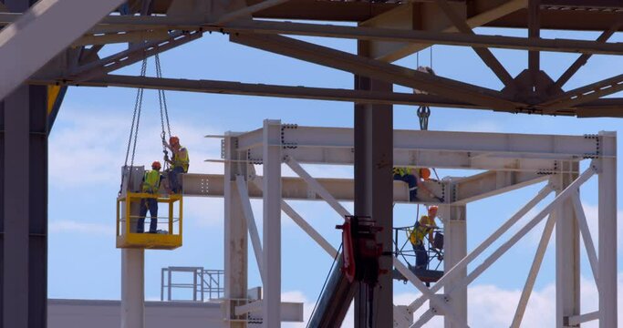 In a workshop under construction, car lifts raise workers in their cradle to the ceiling to perform work there