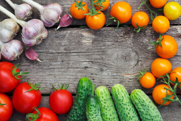 Fresh vegetables on a wooden background with top view. Colorful tomatoes, cucumbers and garlic bulbs on the old grey table with copy space. Natural frame with close up.
