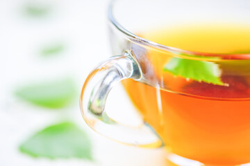 Herbal tea in a glass cup with green leaf. Leaves on a white table around a mug with a drink