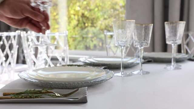 A waiter serves a table in a restaurant. Someone is setting the table in a restaurant. Plates and glasses are placed on the table. The decor of the festive table in gray-silver tones with gold cutlery