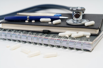 On the table are a notebook, a stethoscope, a pen, pills and a thermometer.