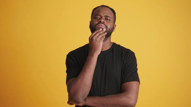 A serious african american man pondering and nodding standing isolated over yellow background