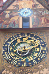 Fototapeta na wymiar antique city hall gable with painted wall, small clock blue, light blue above and big clock with golden arrow and dragon clock hands, Roman numerals and zodiac signs in rings, blue clock face,
