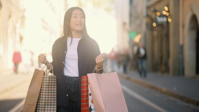 Attractive asian woman walking with shopping bags on city street and looking at the camera in slow motion. Shopping time. High quality 4k footage