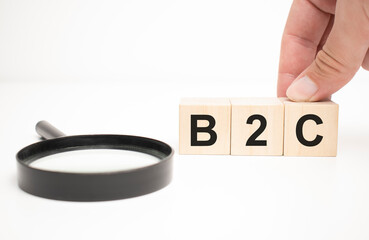 b2c text wooden cube blocks and hand holding magnifying glass on table background.