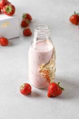 Bottle of strawberry yoghurt or milk on grey table and berry on background