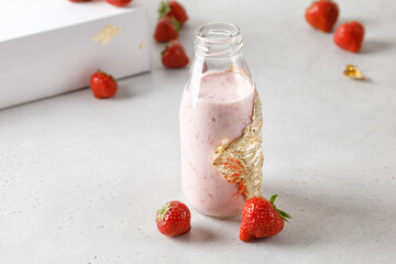 Bottle of strawberry yoghurt or milk on grey table and berry on background