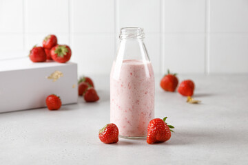 Bottle of strawberry yoghurt or milk on grey table and berry on background
