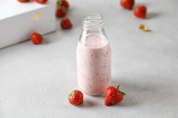 Bottle of strawberry yoghurt or milk on grey table and berry on background
