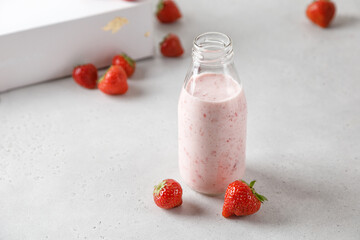 Bottle of strawberry yoghurt or milk on grey table and berry on background