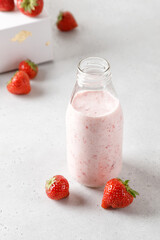 Bottle of strawberry yoghurt or milk on grey table and berry on background