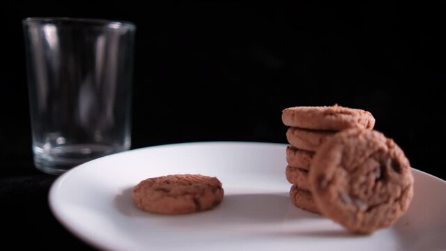 Hand grabbing cookie from a plate next to an empty glass