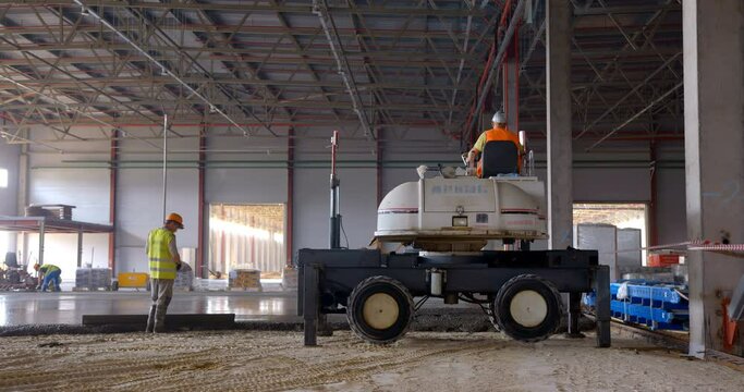 At a construction site in a workshop under construction, industrial wheeled motorized laser leveling device for concrete screed very efficiently makes a concrete floor of a large area
