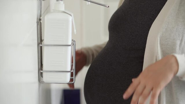 Close Up Young Pregnant Woman Treats Disinfects Hands With Antiseptic Before Medical Control On Hospital. Visit Gynecologist Doctor At Clinic. Examine Expectant Belly Baby Mother Healthcare Check Up