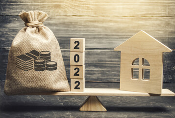 Money bag 2022 and a wooden house on the scales. Real estate concept. Family budget planning....