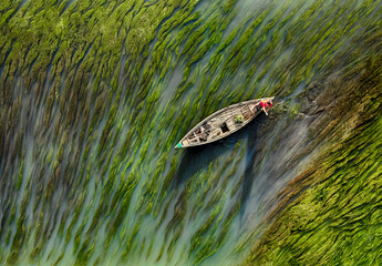 People guide their boats through tranquil, water color-like green reeds and algae on the Karatoya...