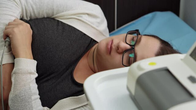 Bespectacled Pregnant Woman On Hospital Couch During Medical Control Cardiotocography. Visit Gynecologist Doctor At Clinic Pregnancy Consultant. Examine Expectant Belly Baby Mother Healthcare Check Up