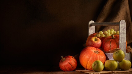 Ripe pumpkins, apples and pears in wooden box on dark brown background with copy space. Thanksgiving background. Autumn harvest