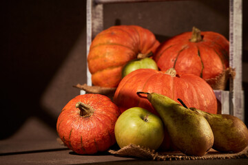 Ripe pumpkins, apples and pears in wooden box on brown background with sinlight. Thanksgiving background. Autumn harvest