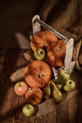 Ripe pumpkins, apples and pears in wooden box on brown background with sunlight. Thanksgiving background. Autumn harvest