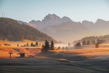 Alpe di Siusi (Seiser Alm) alpine meadow with beautiful foggy sunrise in the background with the...
