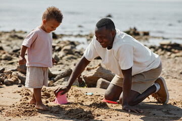 Side view full length portrait of African-American man playing with son on beach together