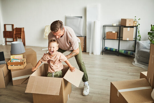 Portrait of father playing with smiling boy in cardboard box while family moving to new house, copy space