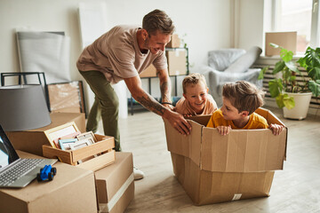 Portrait of modern father playing with two boys in cardboard box while family moving to new house, copy space
