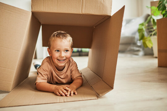 Front view portrait of cute boy playing in cardboard box while family moving to new house, copy space