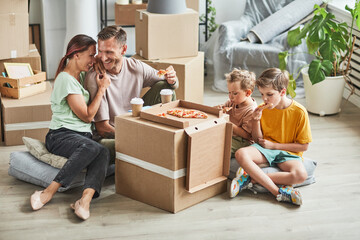 Portrait of happy family eating pizza from cardboard box while celebrating moving in to new house, copy space