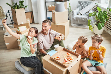 Portrait of happy family eating pizza from cardboard box and taking selfie photo while celebrating...