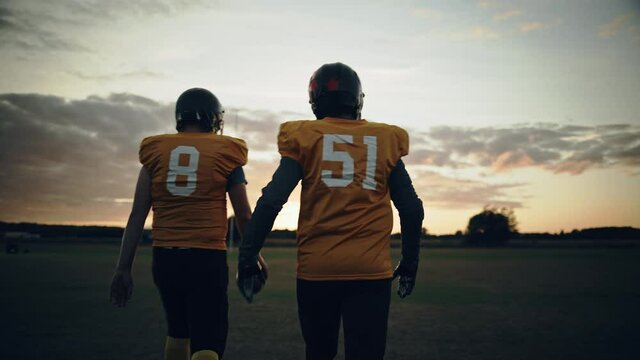 American Football Game Start Teams Ready: Two Professional Players Walk on Field Determined to Win. Competitive Friends Full of Brutal Energy, Power, Skill. Immersive Handheld Following Shot