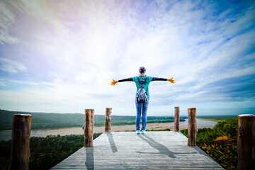 Asian woman standing with hands up achieving looking view sky. Girl welcomes a sun. Successful woman hiker open arms on a sunrise mountain top.