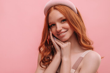Cute redhead model with baby face pressing hands to face against pink blank background. Smiling...