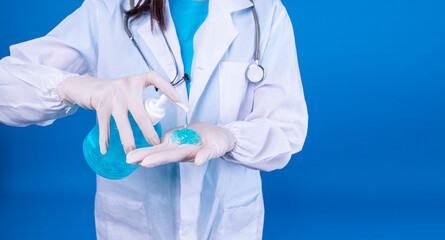 Hand sanitizer, anti bacterial, health care concept. Hands of doctor wear latex gloves with stethoscope holding bottle pump applying blue alcohol gel on own hands over isolated blue background.