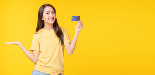Payment purchase and financial concept. Cheerful young woman wearing casual clothes while holding  credit card mockup in own hand while standing with copy space over isolated yellow background.