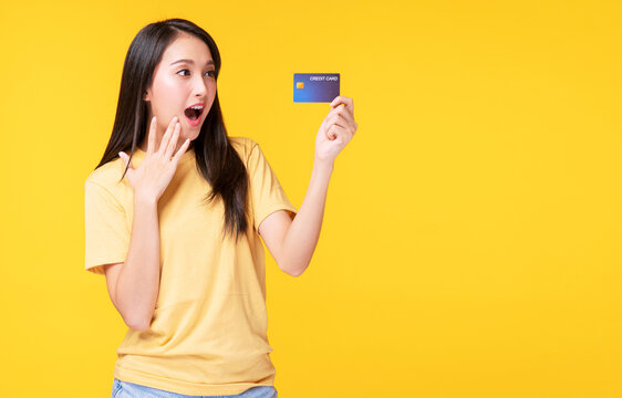 Payment purchase and financial concept. Cheerful young woman wearing casual clothes while holding  credit card mockup in own hand while standing with copy space over isolated yellow background.