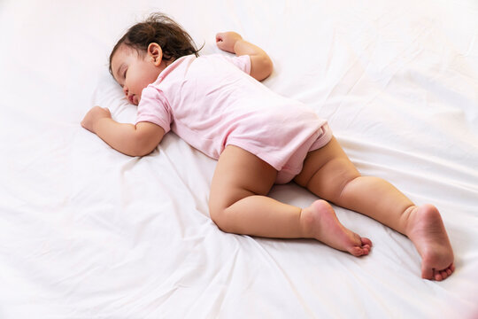 Little Baby Girl 12 Months Wearing Pink Cloth Sleeping On White Bed At Home. Adorable One Year Old Toddler Mixed Race Asleep Having Good Dream Resting In The Bedroom.