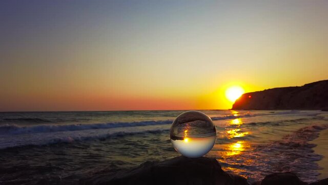 A glass ball stands on a cliff in front of the sea with light waves at sunset - Kos Island, Greece