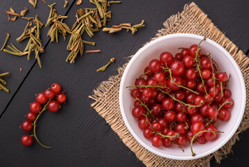 Red currants in a white cup stand on a burlap napkin on a black wooden background. View from above.