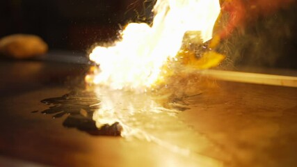 This slow motion video shows that hands of a hibachi chef setting a grill on fire to cook.